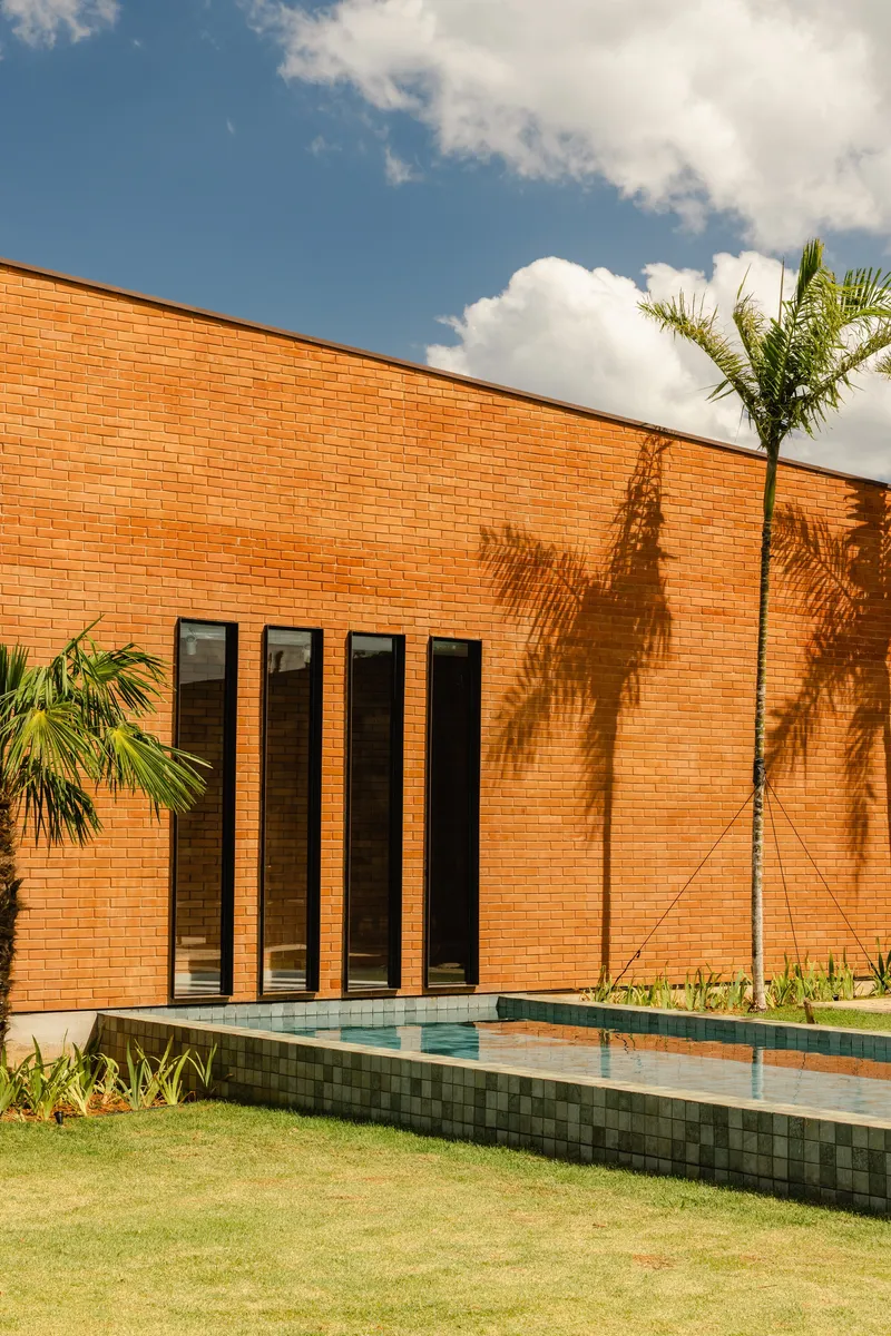 Orange brick facade with four vertical windows beside a raised pool under afternoon sunlight and palms