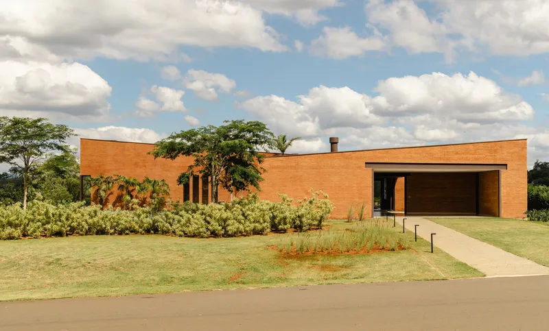 Red brick facade with vertical window slits and recessed timber garage door under white clouds