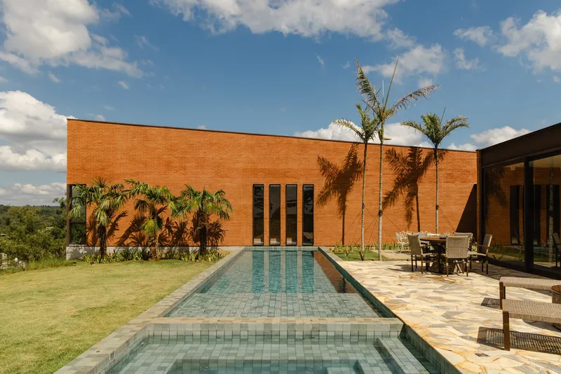 Lap pool with turquoise tile flanked by palms and stone terrace facing brick volume