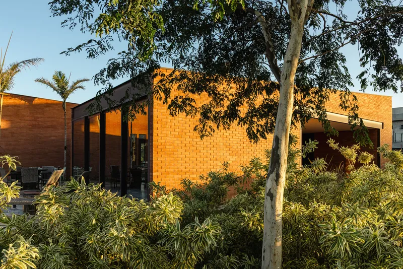 Red brick facade with glazed colonnade seen through landscape palms at golden hour