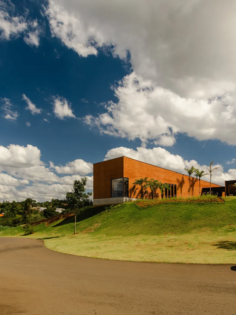 Orange brick volume perched on a sloping grass lawn under a partly cloudy sky