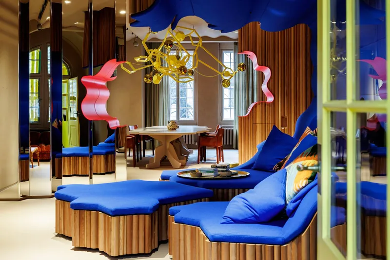 Interior lounge with blue upholstered seating, fluted timber partitions, and brass chandelier under undulating ceiling