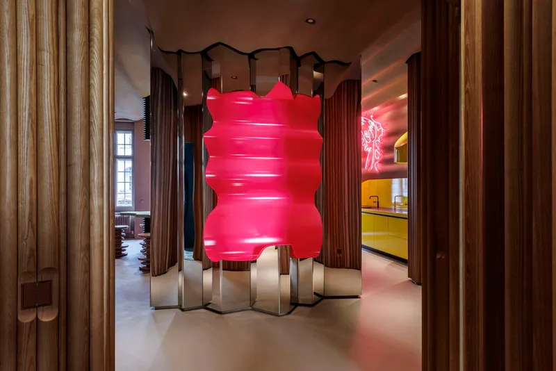 Pink inflatable sculpture on zigzag metal base within timber-clad hallway with views to adjacent rooms