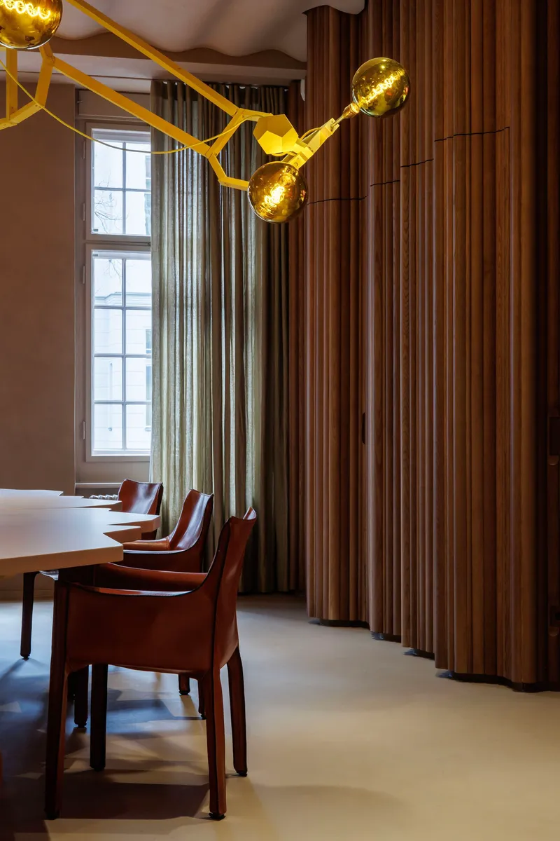 Dining table with leather chairs along fluted timber wall panels beneath gold molecular chandelier near window