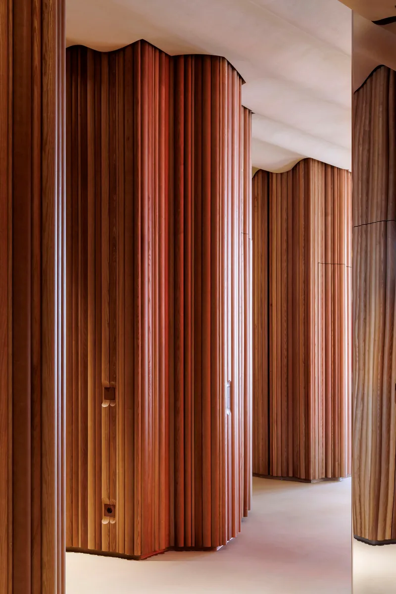 Curved vertical fluted timber wall panels in varying wood tones forming corridor with white ceiling