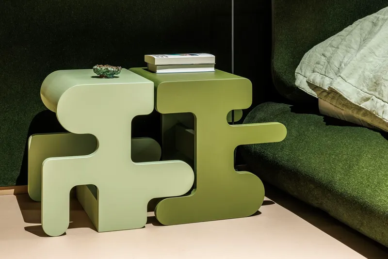 Puzzle-shaped bedside tables in pale green tones next to a dark upholstered headboard