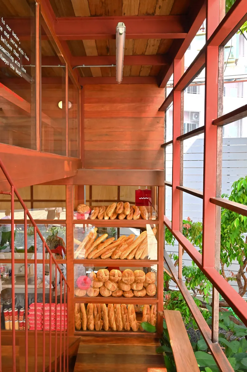 Interior view of red steel-framed bakery display shelves stocked with bread beneath exposed timber ceiling