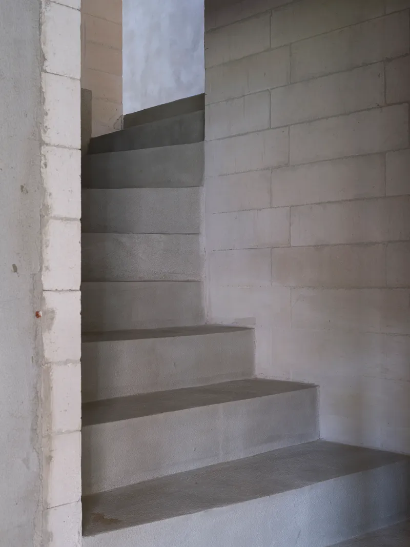 Concrete spiral staircase winding upward through a cylindrical shaft open to cloudy sky