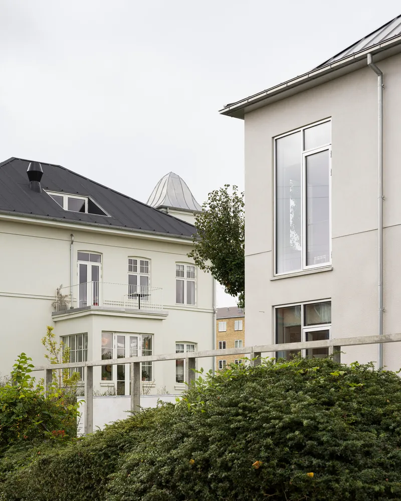 Rear garden view of white rendered facade additions rising above a hedge on an overcast day