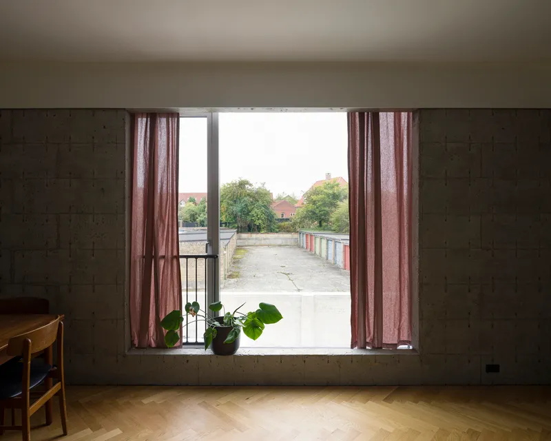 Wide window with pink curtains framing a view of a concrete terrace and distant trees