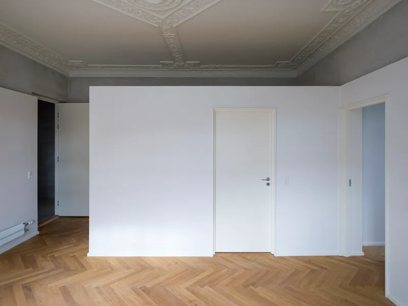Empty room with ornate plaster ceiling molding, herringbone oak floor, and three white doorways