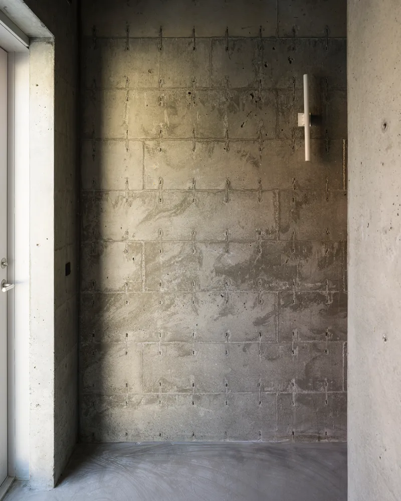 Board-formed concrete wall with tie holes in natural light beside a concrete column and polished floor