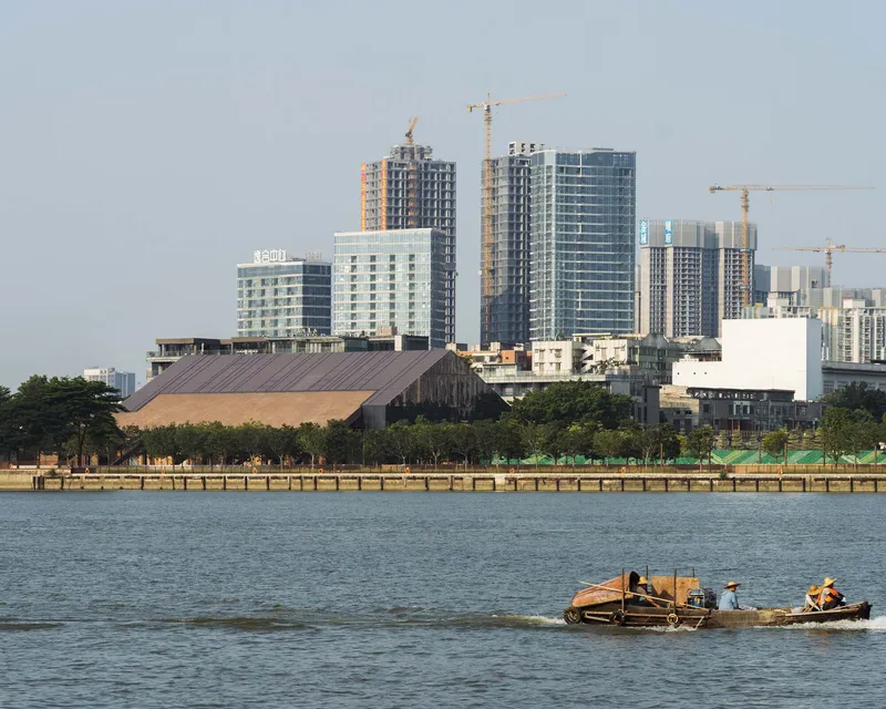 Waterfront view of the timber-clad roof structure against highrise towers under construction