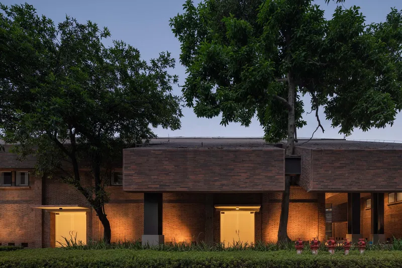 Brick colonnade with interior lighting at dusk, framed by mature trees