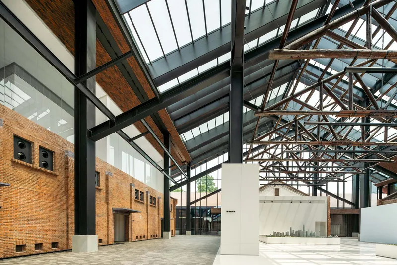 Interior hall with exposed brick walls, steel trusses and glazed skylights above a white display plinth