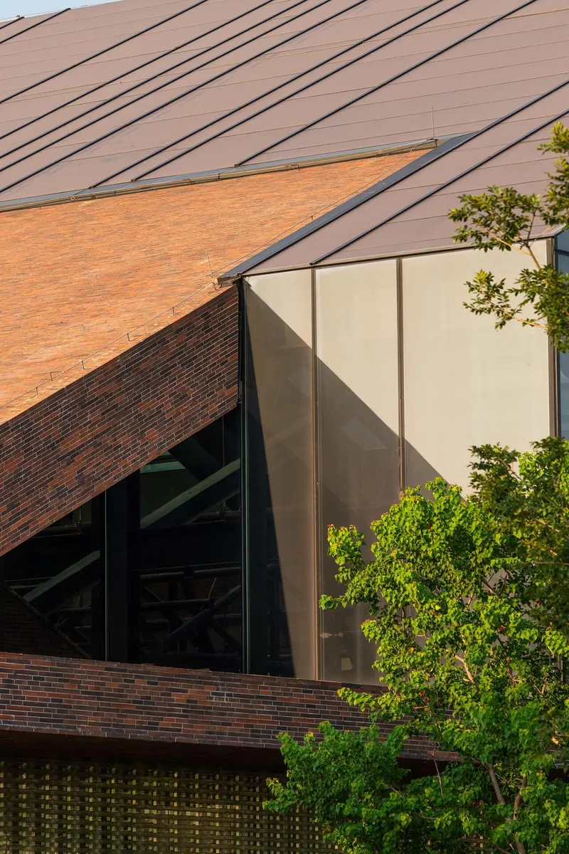 Detail of the sloped metal-seam roof meeting glazed corner panels beside foliage