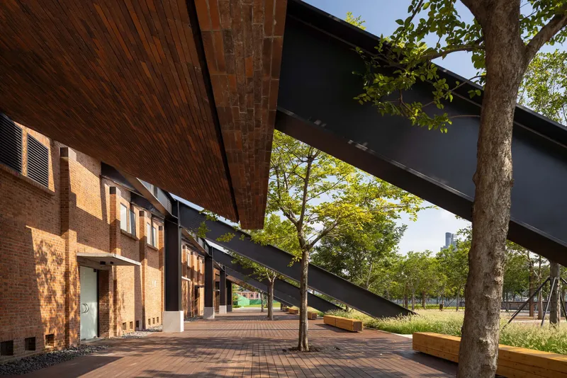 Covered walkway with timber soffit and steel canopy beams extending over brick pavers and mature trees