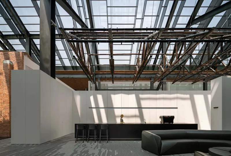 Interior space with exposed steel truss ceiling and glazed roof casting geometric shadows across white walls
