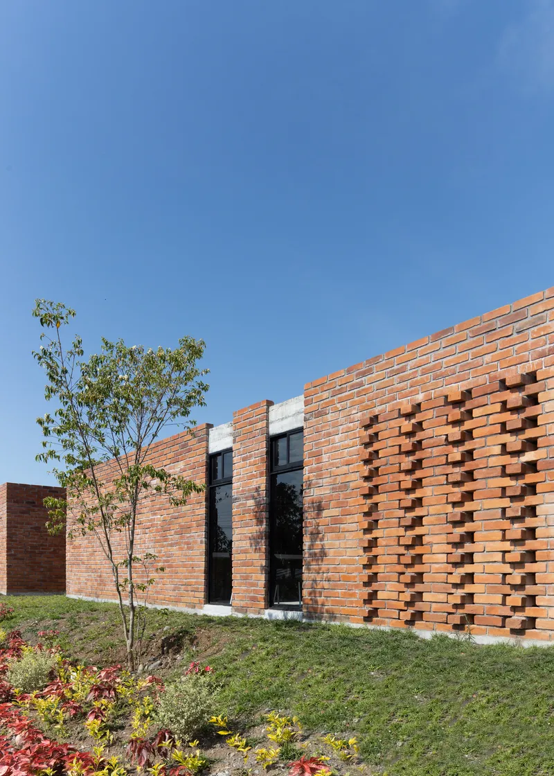 Red brick facade with patterned ventilation openings and planted slope under clear blue sky