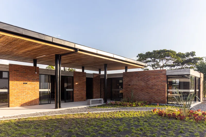 Entry pavilion with extended timber slat roof, steel columns, brick walls, and planted beds at dusk
