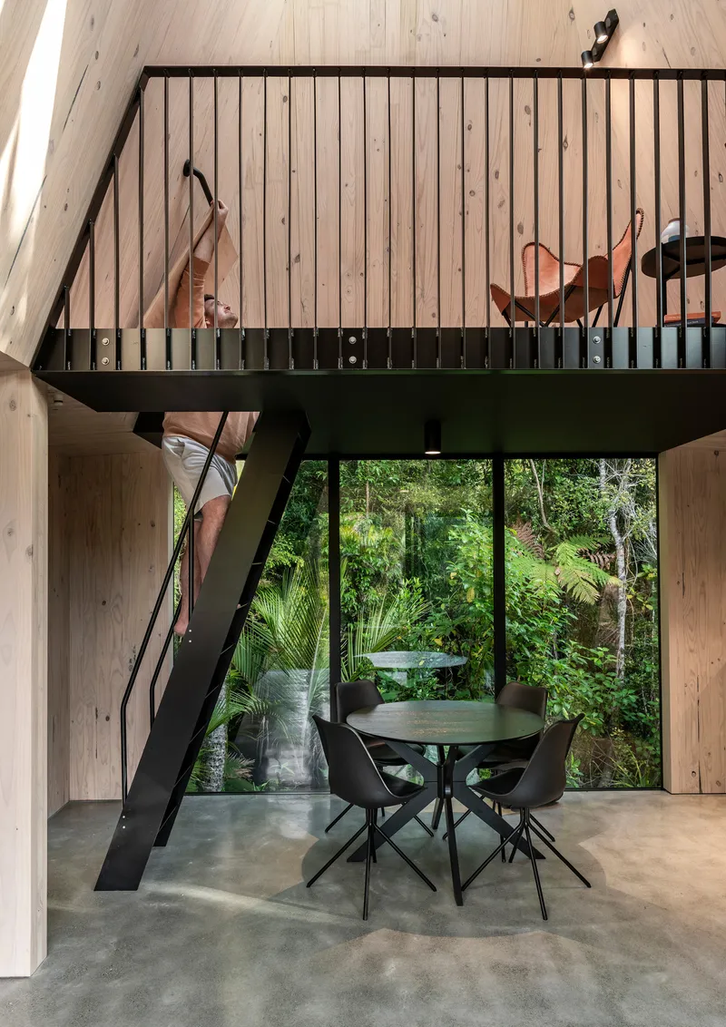 Steel mezzanine with vertical balusters and ship ladder overlooking dining area with glazed wall to garden beyond