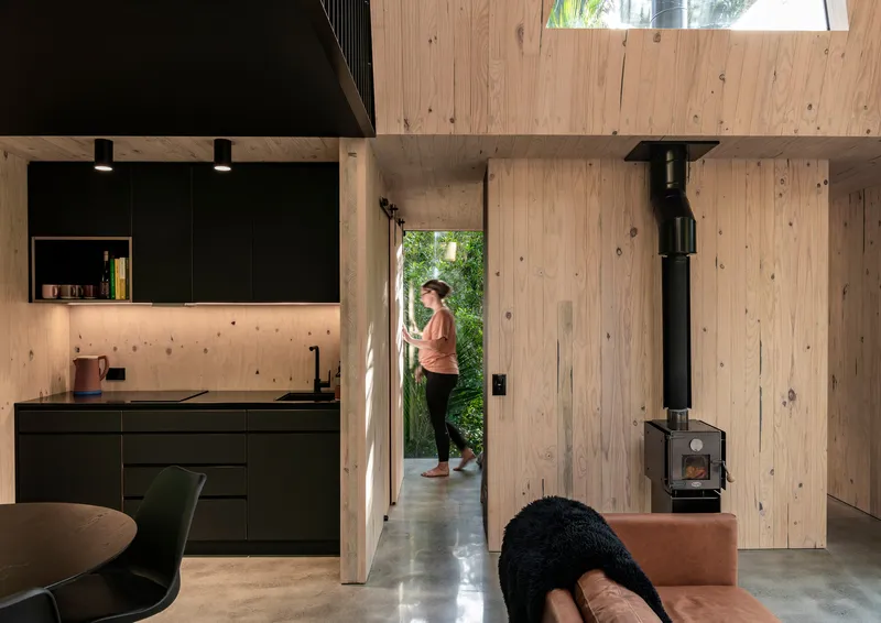 View from living area through open doorway showing person entering from garden with woodstove and kitchen beyond