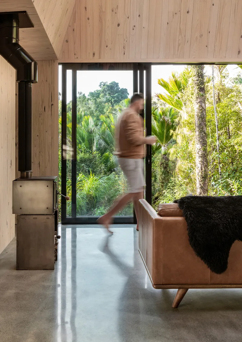 Person in motion crossing polished concrete floor between leather sofa and glazed doors to planted yard