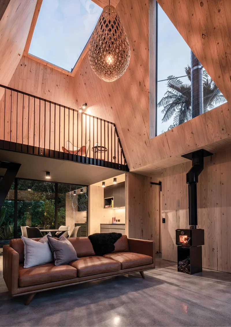 Double-height living space with timber walls, skylight and hanging woven pendant at dusk