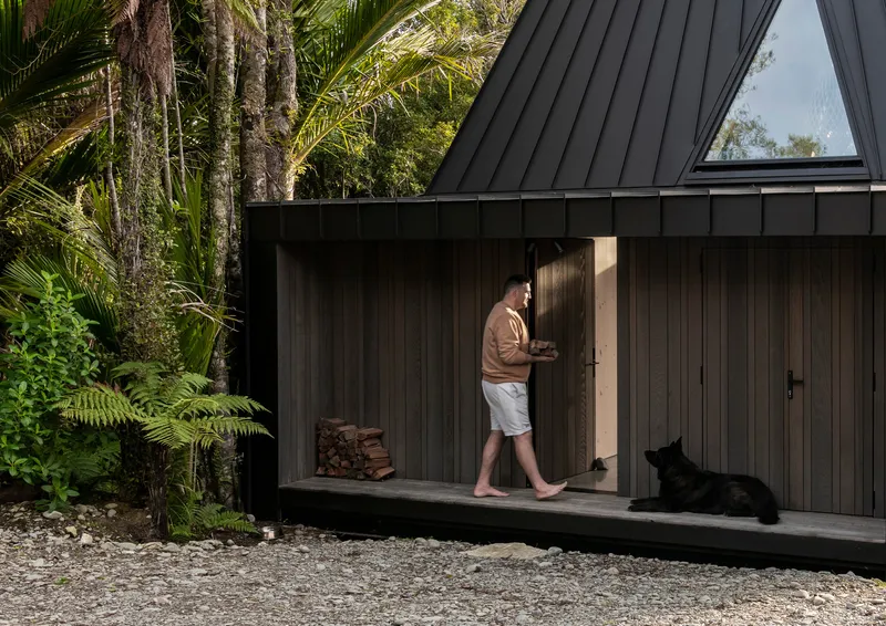 Covered exterior deck with timber cladding and person walking past stacked firewood and resting dog