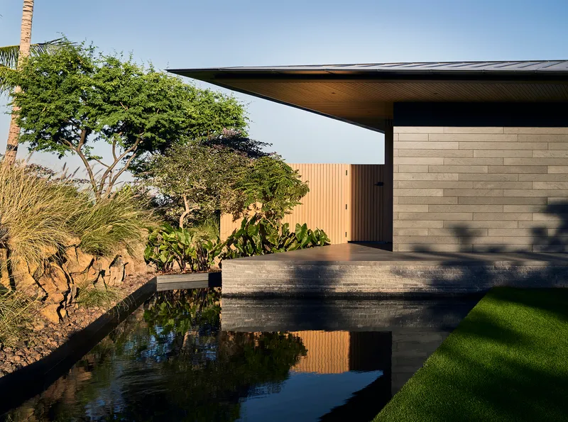 Entry courtyard with reflecting pool, horizontal stone wall, and cantilevered roof casting afternoon shadows
