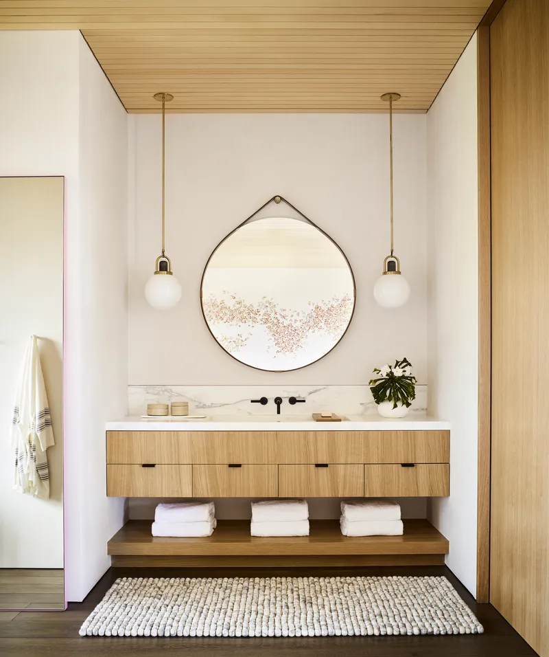 Powder room vanity with timber drawer fronts, circular hanging mirror, and paired pendant lights