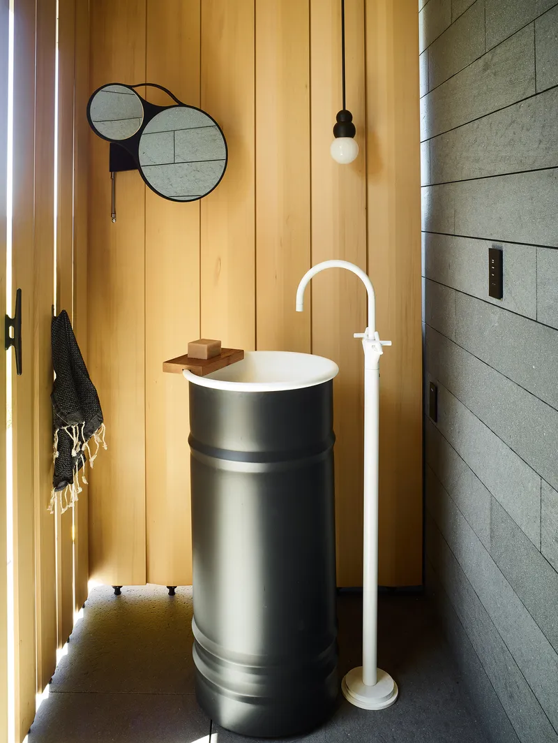 Powder room with cylindrical pedestal sink, vertical timber paneling, and overlapping circular mirrors