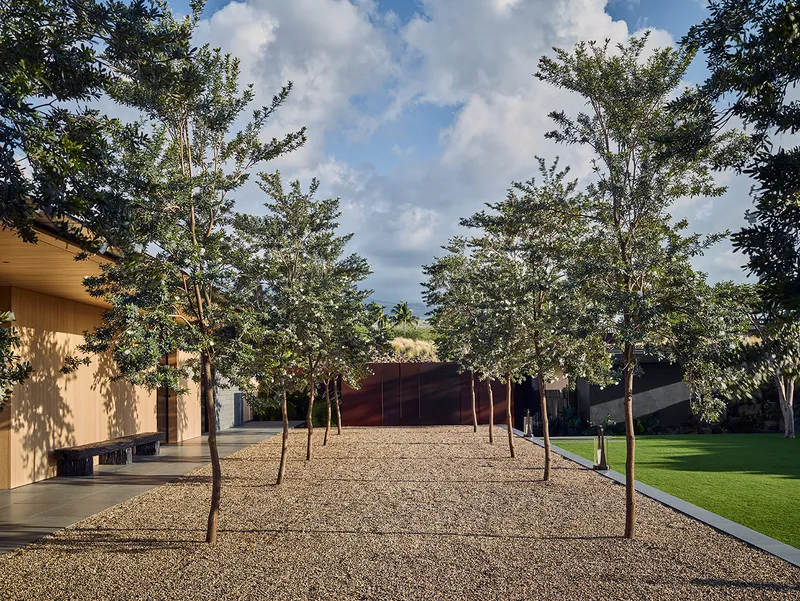 Gravel courtyard lined with trees flanked by low wings under dramatic cloud cover