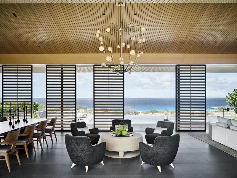 Open plan living space with horizontal louvered screens framing ocean horizon and pendant chandelier