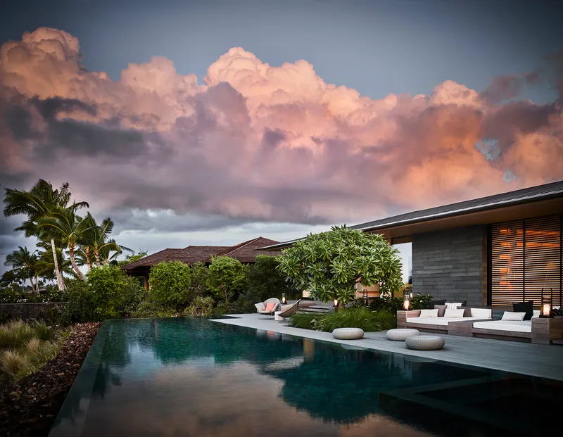 Pool terrace with horizontal louvers and planted beds beneath a dramatic storm cloud formation at dusk