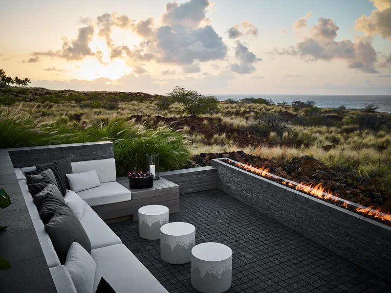 Sunken seating area with linear fire feature and volcanic stone walls facing the ocean at sunset