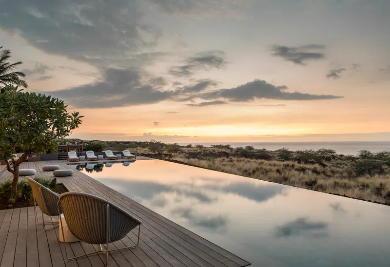 Infinity pool with timber deck overlooking coastal grassland at sunset