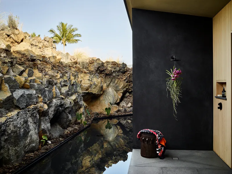 Outdoor shower alcove with black wall against exposed volcanic rock formation