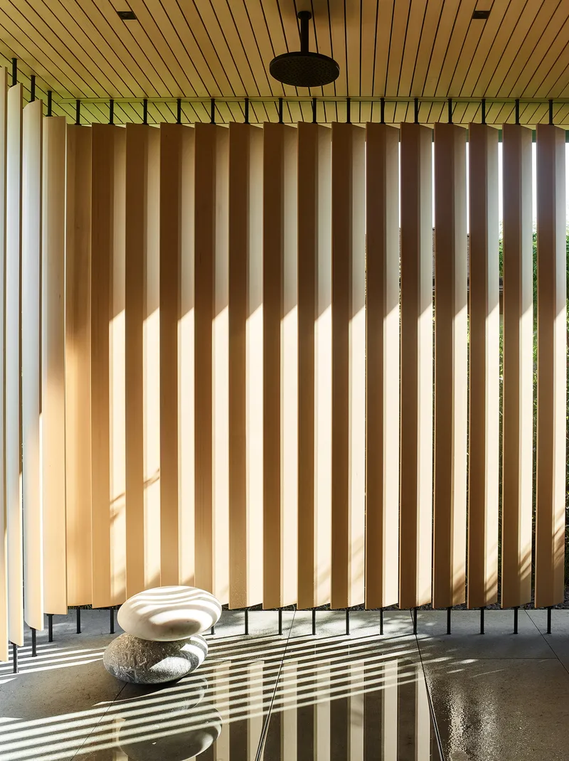 Interior screen of vertical timber slats filtering afternoon light across polished floor