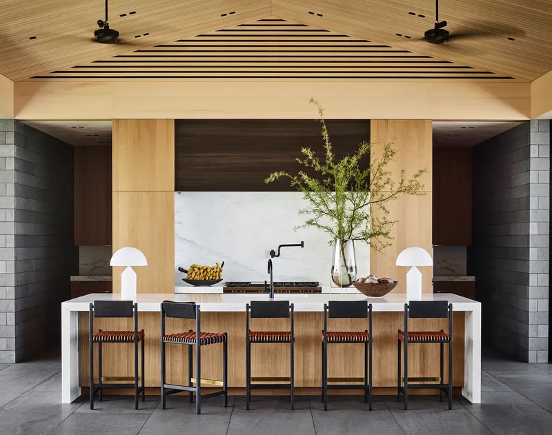 Kitchen island with bar seating beneath vaulted timber ceiling and marble backsplash