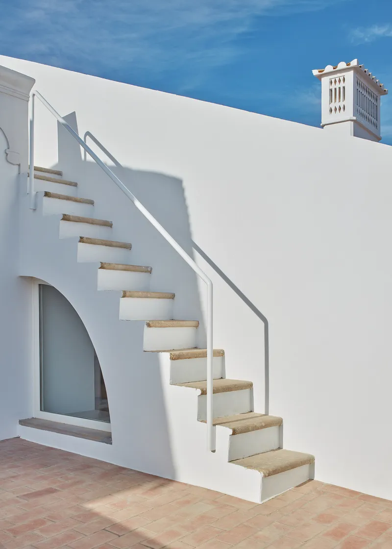 Exterior staircase with stone treads and white stucco wall casting sharp shadows on terracotta paving