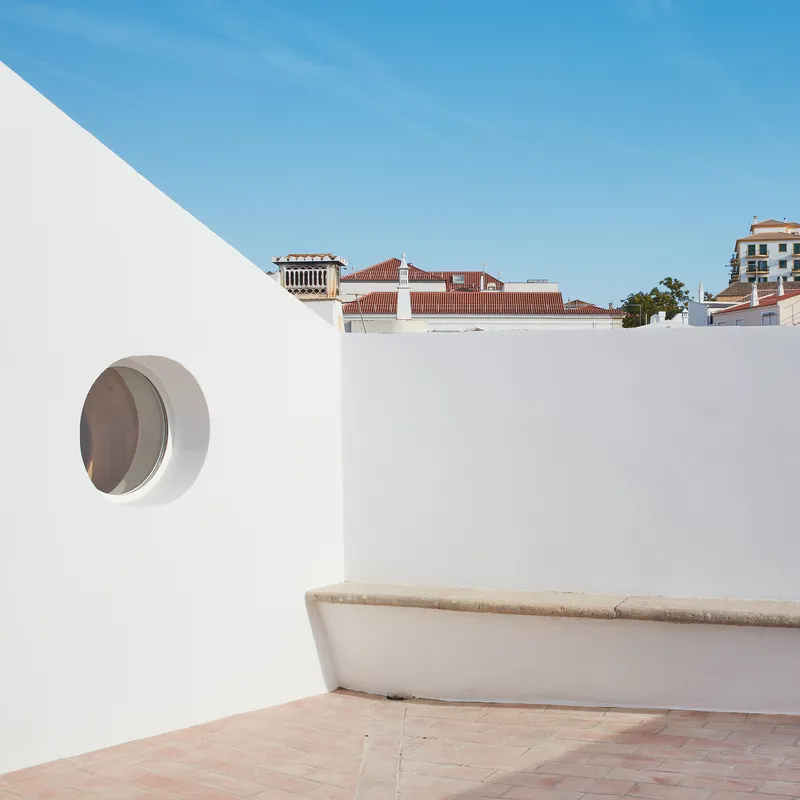 Rooftop terrace with circular window in white wall and terracotta tile roofs visible in background