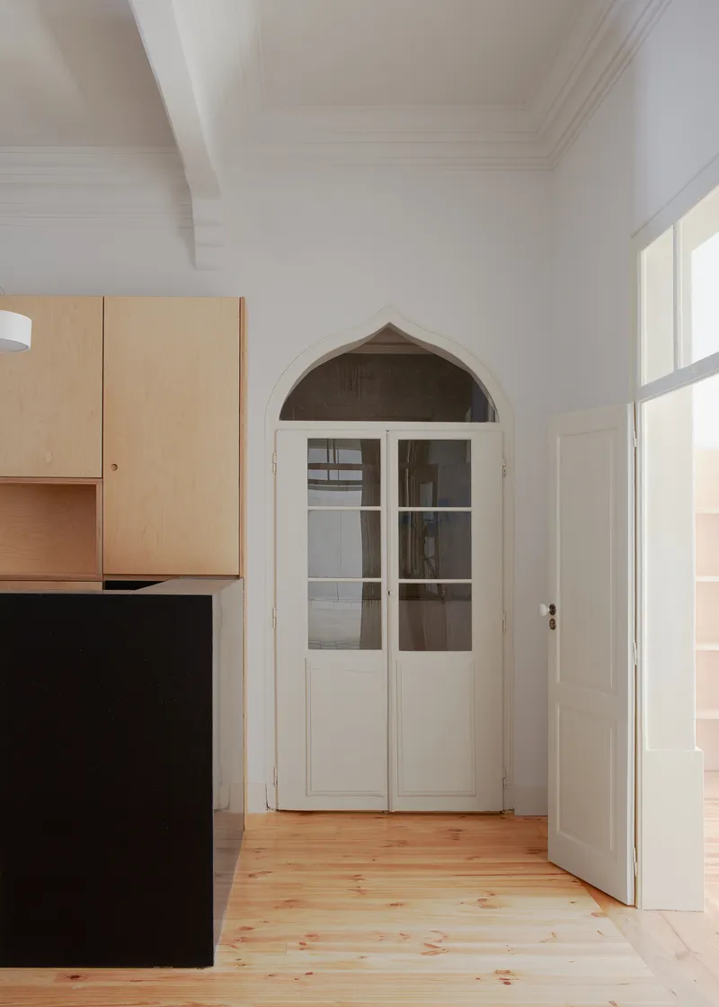 Arched doorway with glazed double doors next to birch plywood cabinets and pine flooring in white room