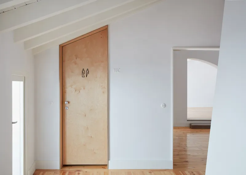 Plywood restroom door with pictogram signage set in white painted walls with exposed ceiling beams