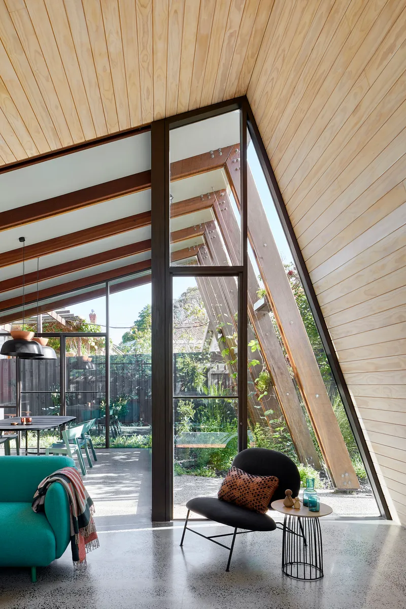 Slanted timber-lined ceiling above glazed corner opening with exposed steel frame and polished concrete floor