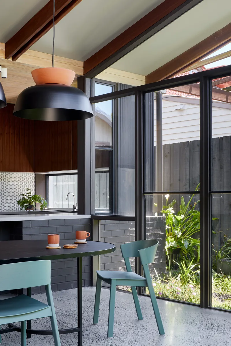 Dining area with exposed timber beams and floor-to-ceiling glazing overlooking planted courtyard in daylight