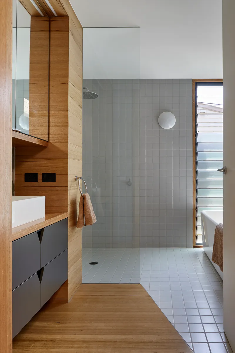 Bathroom with grey tile shower enclosure, timber vanity cabinetry and narrow glazed door to exterior