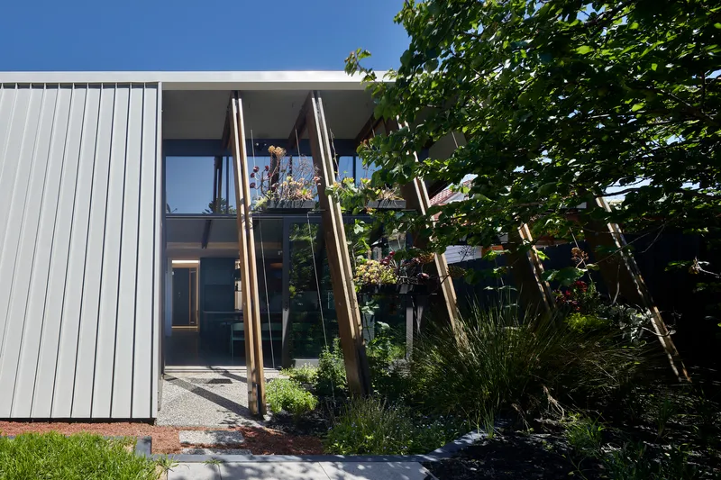 Entrance courtyard with vertical timber posts and plantings framed by white cladding under blue sky