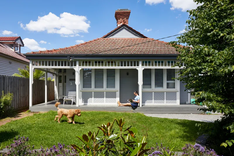 Front elevation of the existing weatherboard cottage with terracotta tile roof, decorative trim and person seated on deck
