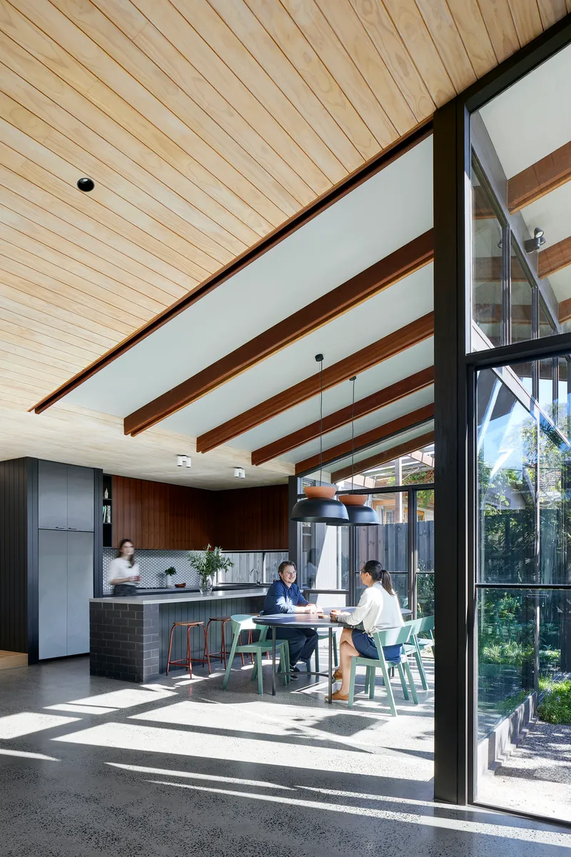 Open-plan kitchen and dining area with exposed timber beams and two people seated at a table